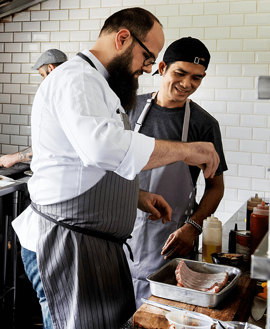 Two cooks sprinkling salt on ribs