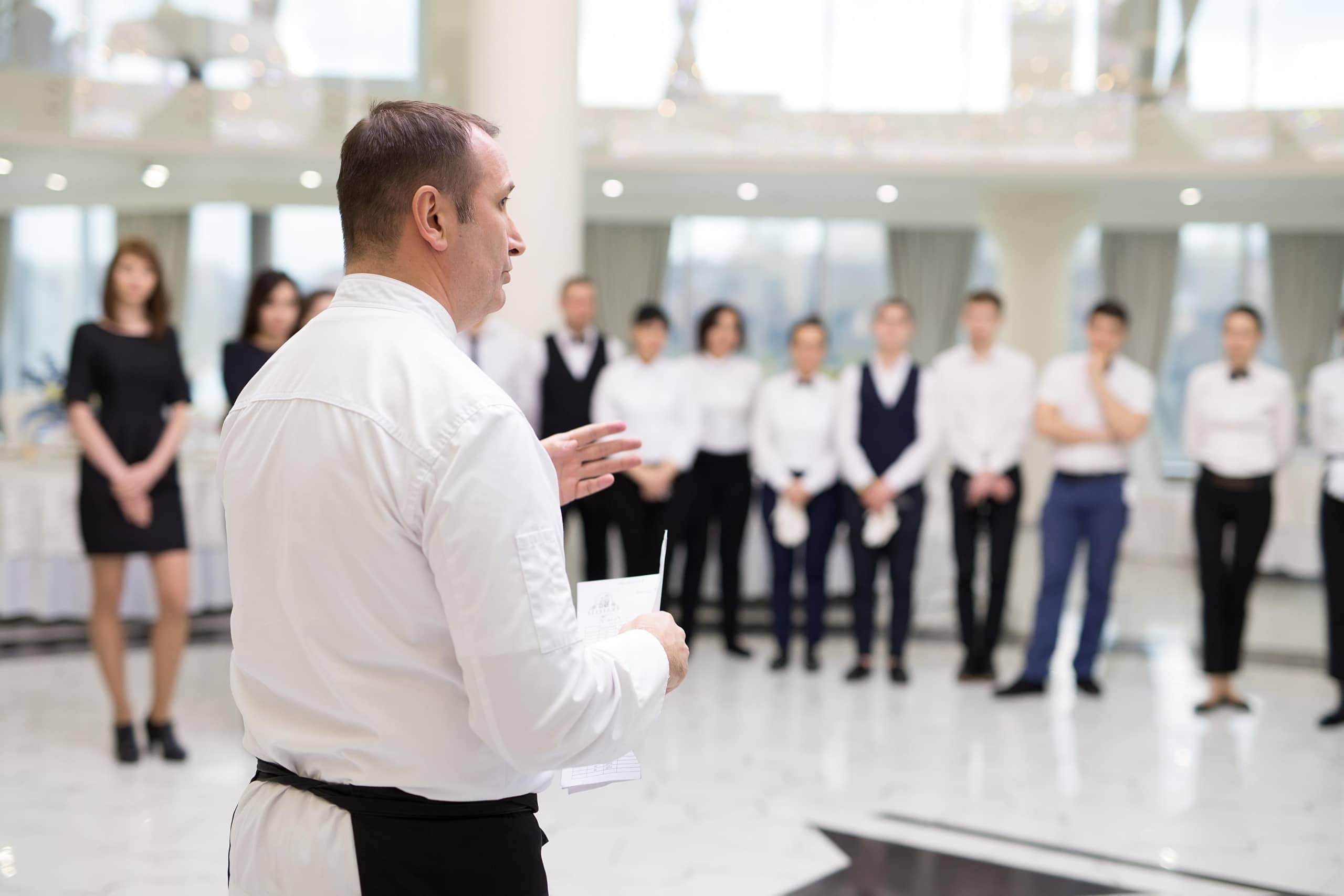 A chef standing in front of a group of professionals talking about food safety.