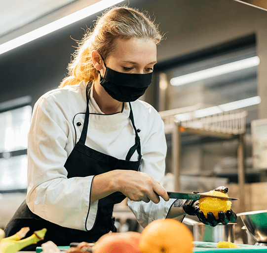 Woman wearing gloves and a mask while cutting a lemon.