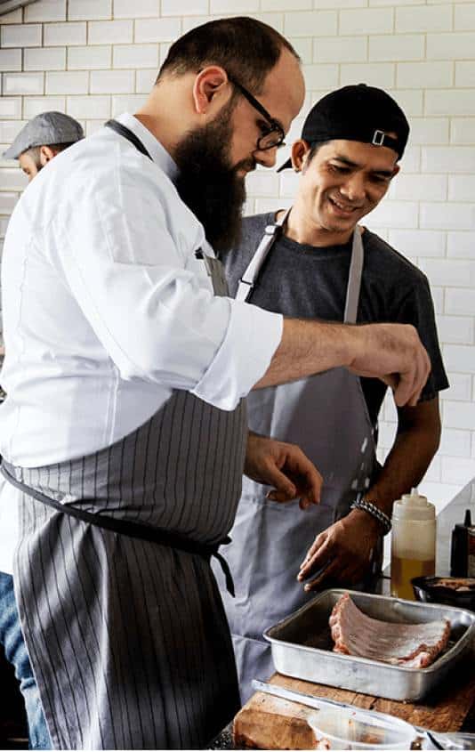 Two cooks sprinkling salt on ribs
